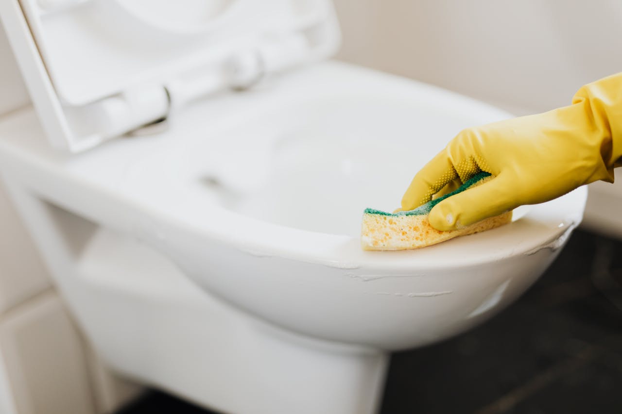 who-we-are Close-up of a gloved hand using a sponge to clean a toilet, focusing on hygiene.