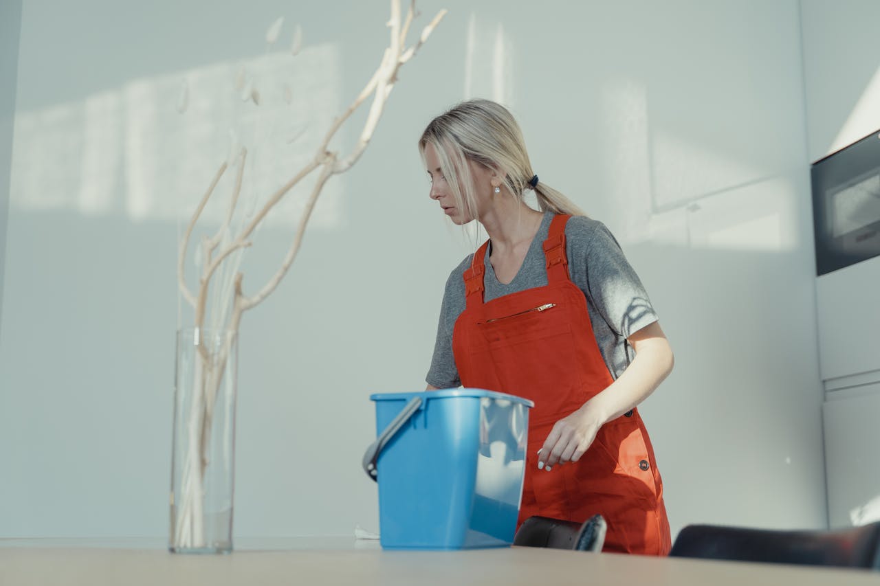 my-steps A woman in a red uniform cleans indoors with a blue bucket, ensuring a spotless environment.